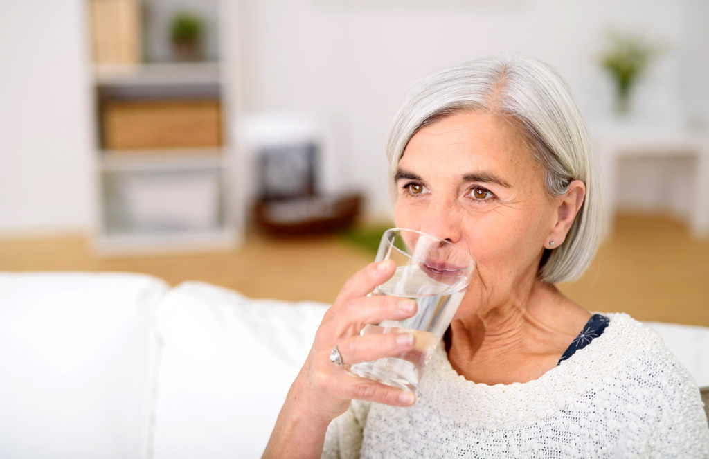 Ältere Frau trinkt aus einem Glas Wasser